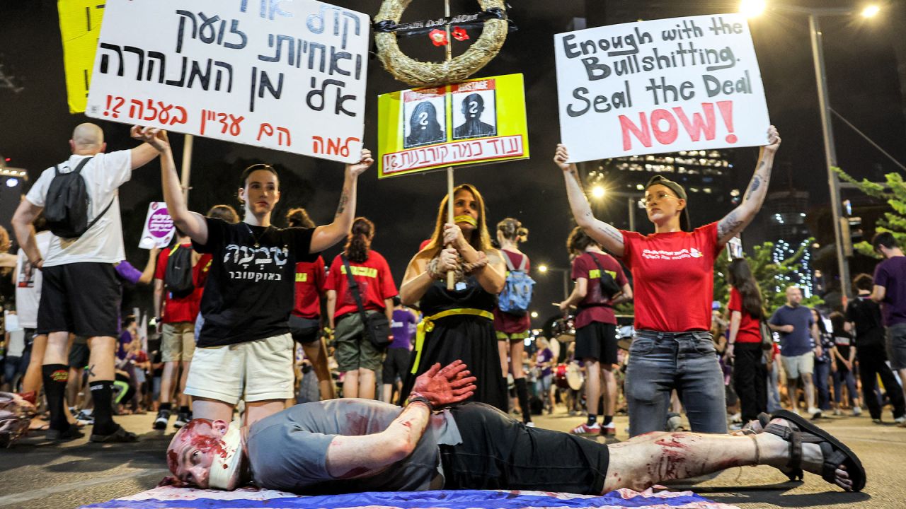 Un manifestante se hace pasar por un rehén israelí que yace en el suelo sobre una bandera mientras otros levantan carteles pidiendo un acuerdo durante una manifestación que exige acciones para liberar a los rehenes israelíes cautivos en la Franja de Gaza desde los ataques del 7 de octubre frente a la sede del Ministerio de Defensa israelí en Tel Aviv en medio del conflicto en curso en el territorio palestino entre Israel y Hamás. | Foto:JACK GUEZ / AFP