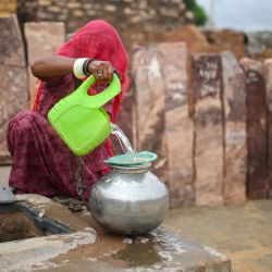 En esta fotografía una mujer con velo llena agua en su casa en la aldea de Sanwata, cerca de Jaisalmer, en el estado desértico de Rajastán, en la India. Las turbinas eólicas que giran en el desierto de Thar, en la India, suministran energía verde fundamental para la nación más poblada del mundo, pero quienes viven a su sombra dicen que esto se produce a costa de ellos. En el estado occidental de Rajastán, donde se encuentra la mayor parte del desierto de Thar, eso incluye la pérdida de tierras de pastoreo y el daño a los bosques sagrados llamados "orans". | Foto:IDREES MOHAMMED / AFP
