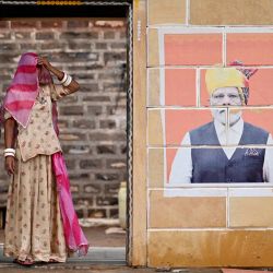En esta fotografía una mujer con velo aparece de pie junto a los murales de B.R. Ambedkar, el arquitecto de la constitución india y del primer ministro indio Narendra Modi, en la aldea de Sanwata, cerca de Jaisalmer, en el estado desértico de Rajastán, en la India. | Foto:IDREES MOHAMMED / AFP