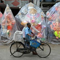 Un hombre empuja su bicicleta junto a ídolos envueltos en plástico de la deidad hindú Ganesha en una calle antes del festival Ganesh Chaturthi, en Chennai, India. | Foto:R. Satish Babu / AFP