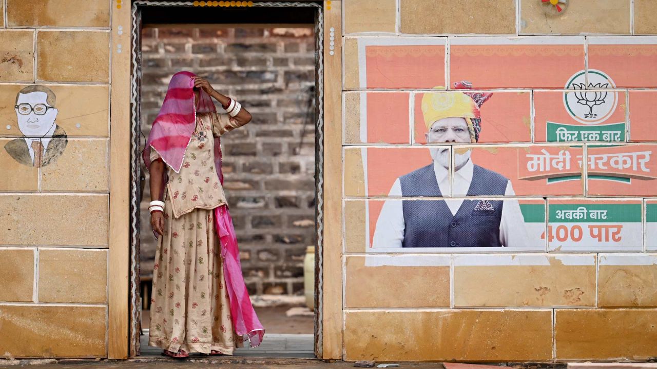 En esta fotografía una mujer con velo aparece de pie junto a los murales de B.R. Ambedkar, el arquitecto de la constitución india y del primer ministro indio Narendra Modi, en la aldea de Sanwata, cerca de Jaisalmer, en el estado desértico de Rajastán, en la India. | Foto:IDREES MOHAMMED / AFP