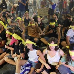 Manifestantes con una venda amarilla en los ojos se sientan en el suelo durante una manifestación antigubernamental que exige la liberación de los israelíes retenidos como rehenes por militantes palestinos en Gaza desde octubre, en Tel Aviv. | Foto:JACK GUEZ / AFP