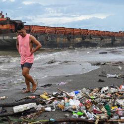 Los residentes caminan por la orilla mientras se ve una barcaza arrastrada por la tormenta tropical Yagi en Rosario, provincia de Cavite. Las inundaciones y los deslizamientos de tierra mataron a 11 personas después de que una feroz tormenta tropical arrojara fuertes lluvias en Filipinas por segundo día, dijeron las autoridades. | Foto:JAM STA ROSA / AFP