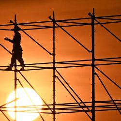 Los trabajadores se encuentran en un andamio al atardecer en Hanoi, Vietnam. | Foto:NHAC NGUYEN / AFP