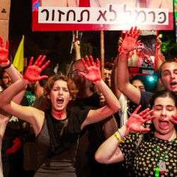 Manifestantes con las manos pintadas de rojo corearon consignas durante una protesta contra el gobierno para pedir la liberación de los rehenes que se encuentran cautivos desde los ataques del 7 de octubre por parte de militantes palestinos en la Franja de Gaza y un acuerdo para liberarlos, cerca de la residencia del primer ministro israelí en Jerusalén, en medio de la guerra en curso en el territorio palestino entre Israel y Hamás. | Foto:MENAHEM KAHANA / AFP