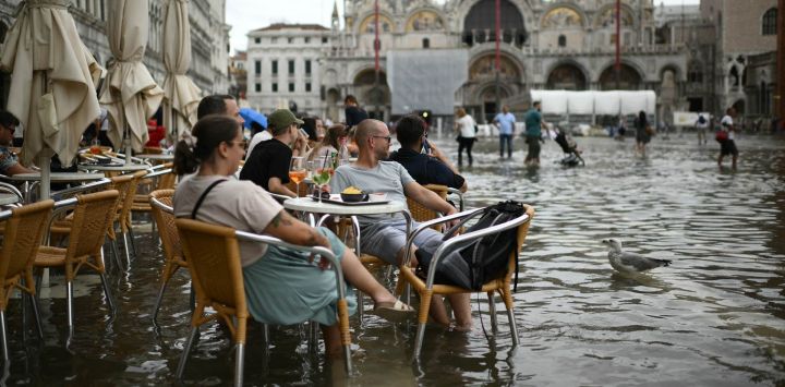 La gente se sienta en la terraza de un café en la plaza de San Marcos inundada durante la marea alta en Venecia.