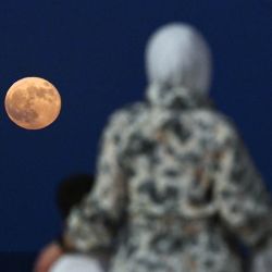 Una mujer con dos niños observa la superluna de la cosecha que se alza sobre las aguas del Golfo frente a la costa de la ciudad de Kuwait. | Foto:Yasser Al-Zayyat / AFP