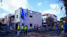 Hombres israelíes cuelgan una bandera israelí sobre un edificio dañado que fue alcanzado por un cohete desde el Líbano