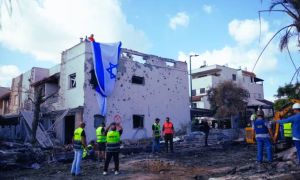 Hombres israelíes cuelgan una bandera israelí sobre un edificio dañado que fue alcanzado por un cohete desde el Líbano