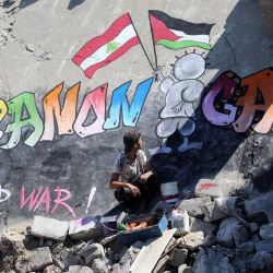 Un joven palestino se sienta junto a un mural que pintó en el tejado de una casa destruida en Khan Yunis, en el sur de la Franja de Gaza, para mostrar su solidaridad con el pueblo de Gaza y el Líbano. El Líbano se enfrenta a la perspectiva de una guerra total entre Israel y Hezbolá, que se han estado disparando casi a diario desde que estalló la guerra en Gaza en octubre. | Foto:Eyad Baba / AFP