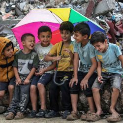 Unos chicos se reúnen bajo un paraguas mientras se sientan junto a los escombros de un edificio derrumbado en el campamento de refugiados palestinos de Bureij. Foto de Eyad BABA / AFP | Foto:AFP