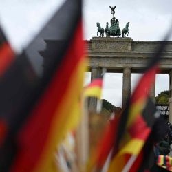 Banderas alemanas se venden en un puesto frente a la emblemática Puerta de Brandeburgo en Berlín en el 34 aniversario de la Unificación de Alemania. Foto de RALF HIRSCHBERGER / AFP | Foto:AFP
