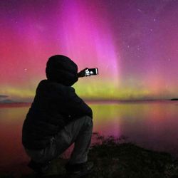 Un hombre toma fotografías de la Aurora Australis, también conocida como Luces del Sur, mientras brilla en el horizonte sobre las aguas del lago Ellesmere. Foto de Sanka Vidanagama / AFP | Foto:AFP