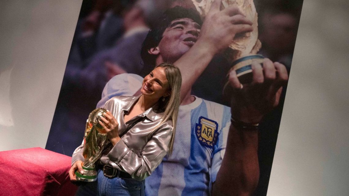 A journalist poses next to a photograph of former Argentina's footballer Diego Maradona holding the trophy of the FIFA World Cup Mexico '86 during a press presentation of the ‘Diego Vive’ theme park, dedicated to Diego Maradona and offering activities echoing Argentinian football legend's life and achievements, in Barcelona on October 8, 2024. 