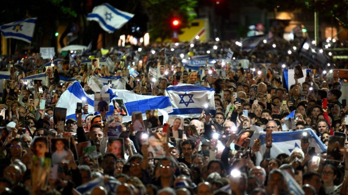 People light their mobile phones and hold Israeli flags during a ceremony organised by the Jewish community in commemoration for the victims of the Hamas attack on October 7 last year within the framework of the first anniversary of the Israel-Hamas conflict at the Jewish community centre of the Mutual Israelite Association of Argentina (AMIA) in Buenos Aires on October 7, 2024. 