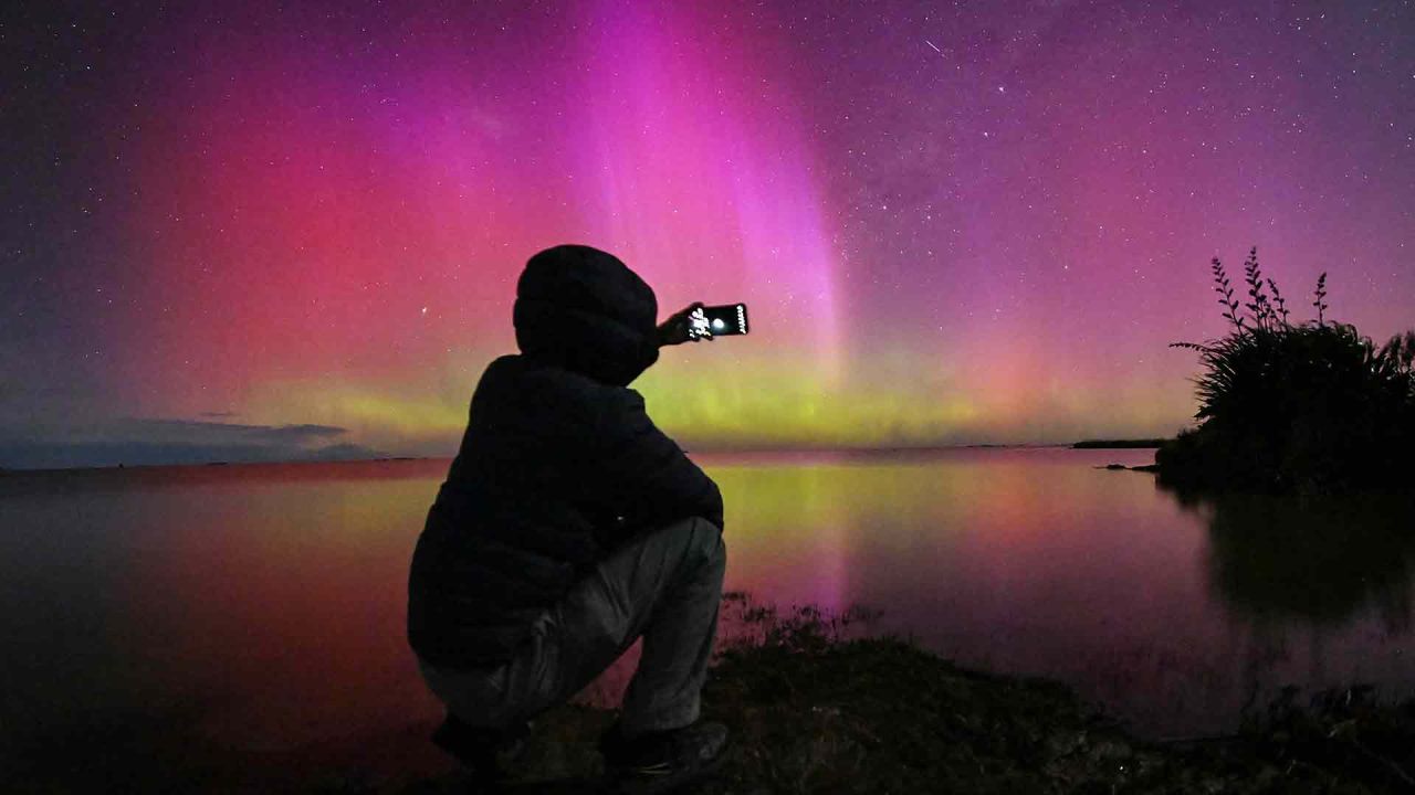 Un hombre toma fotografías de la Aurora Australis, también conocida como Luces del Sur, mientras brilla en el horizonte sobre las aguas del lago Ellesmere. Foto de Sanka Vidanagama / AFP | Foto:AFP