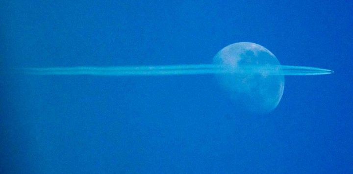 Las estelas de condensación de un avión de pasajeros se ven mientras vuela frente a la Luna en el cielo brumoso sobre Viena, Austria. Foto de JOE KLAMAR / AFP