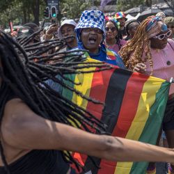 Los asistentes sostienen banderas de Zimbabue y Uganda en solidaridad mientras bailan durante la edición 2024 del Orgullo de Johannesburgo, Sudáfrica. | Foto:MARCO LONGARI / AFP