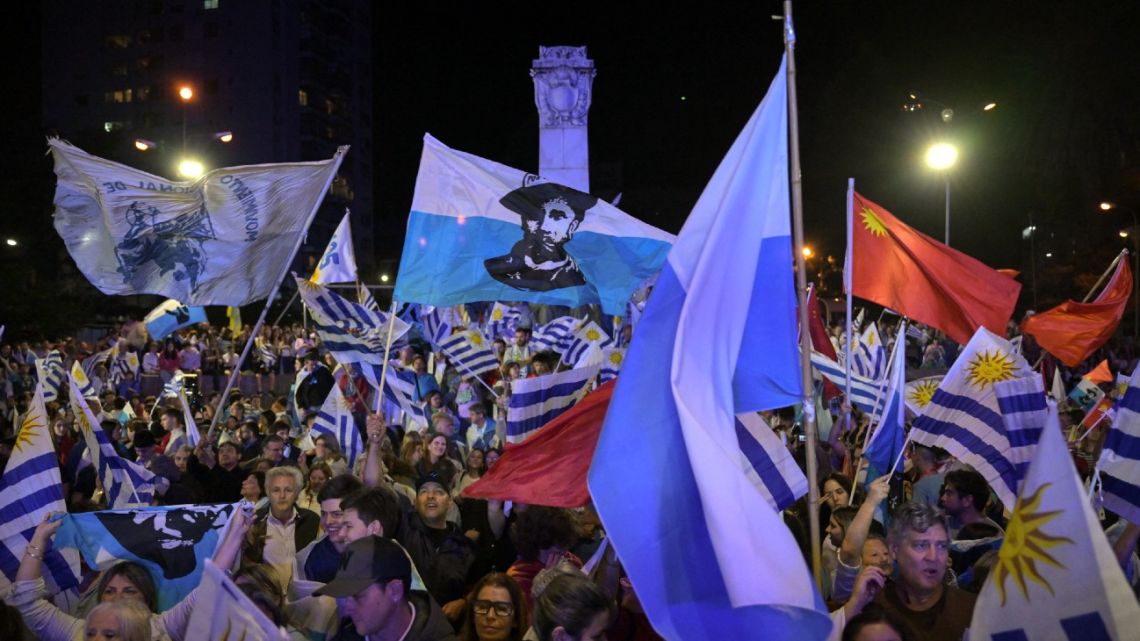 Supporters of parties of the Republican Coalition wave flags as Uruguay's presidential candidate for the Partido Nacional (National Party), Alvaro Delgado (out of frame), speaks during a celebration of the ruling center-right coalition after partial results of the presidential and legislative election were announced, at Plaza Varela Square in Montevideo on October 27, 2024.