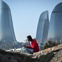 Una mujer sentada frente a las Torres de la Llama, uno de los puntos de referencia del centro de Bakú, en vísperas de la Conferencia de las Naciones Unidas sobre el Cambio Climático de 2024 (COP 29 de la CMNUCC) que se celebrará del 11 al 22 de noviembre de 2024 en Bakú. | Foto:Alexander Nemenov / AFP