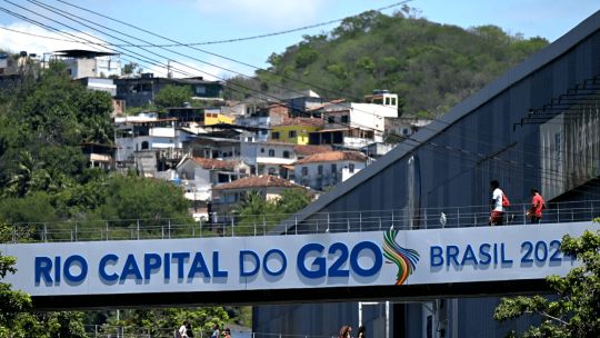 A G20 Summit banner is displayed on a pedestrian bridge in front of Mangueira favela