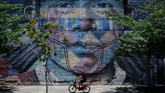 A man on a bicycle rides past grafitti made by Brazilian artist Kobra 