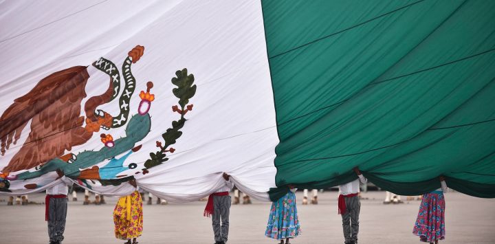 Miembros del ejército mexicano vestidos como soldados revolucionarios sostienen la bandera nacional durante la conmemoración del 114 aniversario de la Revolución Mexicana en la plaza del Zócalo de la Ciudad de México.