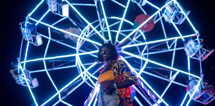 Una mujer se encuentra de pie frente a una noria mientras asiste al tercer día del Festival Nyege Nyege en Jinja, Uganda.