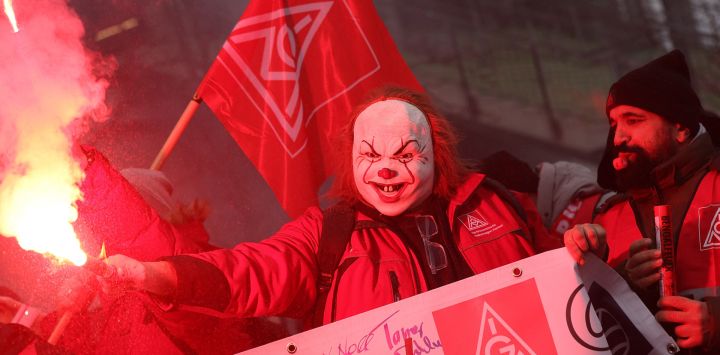 Un participante enmascarado enciende una bengala durante una manifestación de empleados del fabricante de automóviles alemán Volkswagen convocada por el sindicato de trabajadores metalúrgicos IG-Metall en la planta de Volkswagen en Wolfsburg, norte de Alemania, durante una tercera ronda de negociaciones entre la dirección y los representantes de los trabajadores sobre un nuevo acuerdo para la empresa afectada por la crisis.