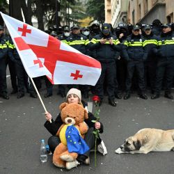 Una mujer sostiene una rosa roja y una bandera georgiana mientras se enfrenta a agentes de policía durante una protesta contra los resultados de las elecciones parlamentarias del mes pasado en Tbilisi, cuando el Parlamento convoca su primera sesión. | Foto:VANO SHLAMOV / AFP