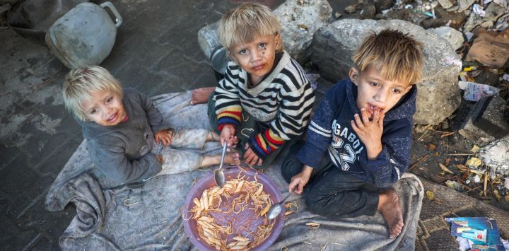 Niños palestinos comparten un plato de comida en su tienda de campaña para desplazados en el campo de refugiados de Bureij, en el centro de la Franja de Gaza, en medio de la guerra en curso entre Israel y el grupo militante palestino Hamás.