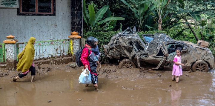 Una familia camina por el barro y pasa junto a un automóvil aplastado tras los deslizamientos de tierra en la aldea Semangat Gunung en Karo, en el norte de Sumatra. Las inundaciones repentinas y un deslizamiento de tierra arrasaron cuatro distritos de la isla indonesia de Sumatra durante el fin de semana, matando al menos a 16 personas, dijo la agencia nacional de desastres.