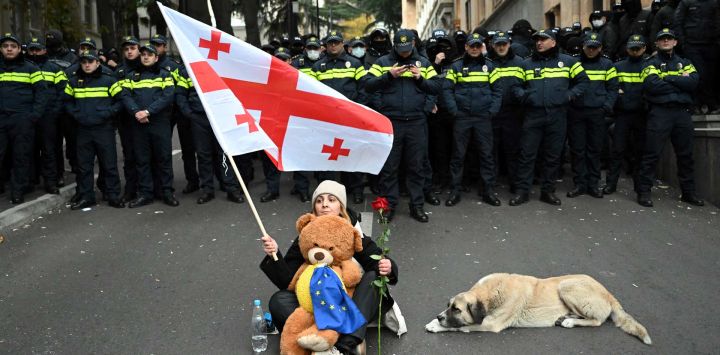 Una mujer sostiene una rosa roja y una bandera georgiana mientras se enfrenta a agentes de policía durante una protesta contra los resultados de las elecciones parlamentarias del mes pasado en Tbilisi, cuando el Parlamento convoca su primera sesión.