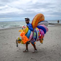 Un vendedor camina en la playa El Yaque en la isla de Margarita, estado Nueva Esparta, Venezuela. Margarita, la principal isla de Venezuela, es un paraíso caribeño en decadencia tras años de devaluaciones, inflación, pandemia y colapso de los servicios públicos. | Foto:JUAN BARRETO / AFP