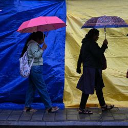 Personas con paraguas caminan por una calle mientras llueve debido a la influencia del ciclón Fengal, en Bengaluru, India. | Foto:IDREES MOHAMMED / AFP