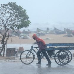 Un hombre tira de su carreta de tres ruedas en medio de fuertes vientos y lluvias en la playa Marina Beach en Chennai, antes de que el ciclón Fengal toque tierra en el estado de Tamil Nadu, en la India. | Foto:R. Satish Babu / AFP