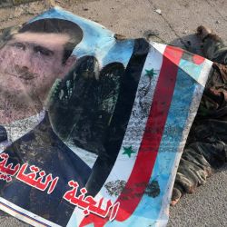 El cuerpo de un soldado del ejército sirio asesinado está cubierto con un cartel del expresidente sirio Bashar al-Assad en una calle de la ciudad capturada de Hama, en el centro-oeste del país. | Foto:MUHAMMAD HAJ KADOUR / AFP
