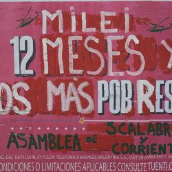 La gente pasa junto a un anuncio callejero intervenido por la "Asamblea de Scalabrini Ortiz y Corrientes" contra el gobierno del presidente argentino Javier Milei que dice: "Milei, 12 meses y somos más pobres", en el primer aniversario del gobierno de Milei en Buenos Aires. | Foto:Juan Mabromata / AFP)
