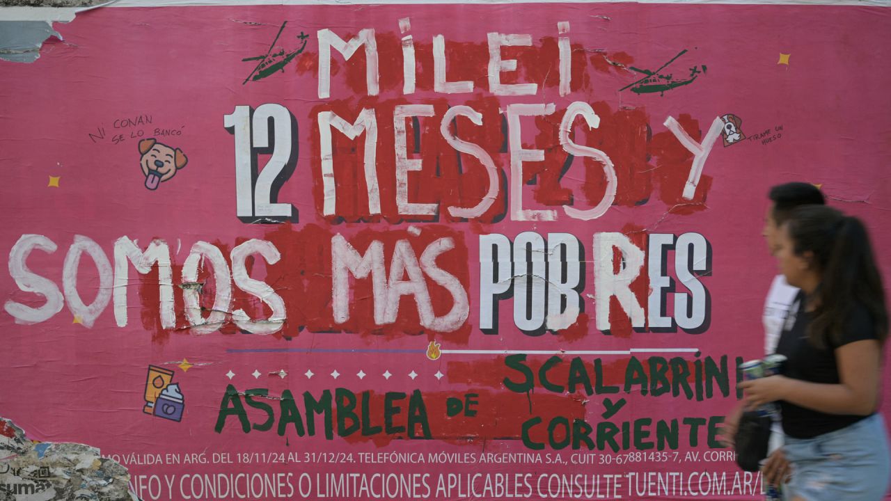 La gente pasa junto a un anuncio callejero intervenido por la "Asamblea de Scalabrini Ortiz y Corrientes" contra el gobierno del presidente argentino Javier Milei que dice: "Milei, 12 meses y somos más pobres", en el primer aniversario del gobierno de Milei en Buenos Aires. | Foto:Juan Mabromata / AFP)