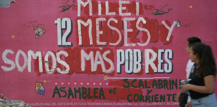 La gente pasa junto a un anuncio callejero intervenido por la "Asamblea de Scalabrini Ortiz y Corrientes" contra el gobierno del presidente argentino Javier Milei que dice: "Milei, 12 meses y somos más pobres", en el primer aniversario del gobierno de Milei en Buenos Aires.