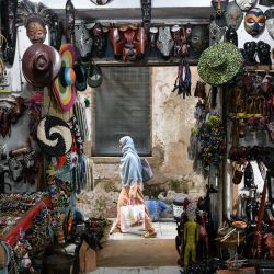 Imagen de una mujer caminando frente a una tienda de recuerdos, en el Stone Town de Zanzíbar, Tanzania. Reconocida por su impresionante belleza natural y su rica historia, Zanzíbar se ha convertido en un destino turístico popular en la región de Africa Oriental. | Foto:Xinhua/Han Xu
