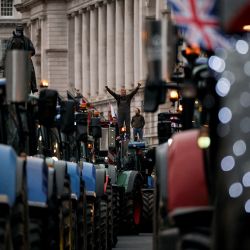 Un agricultor se encuentra sobre el techo de un tractor estacionado a lo largo de Whitehall durante una manifestación para detener “la muerte de la agricultura británica”, en protesta contra los cambios en las reglas del impuesto a la herencia para la propiedad de la tierra de los agricultores, en el centro de Londres. | Foto:BENJAMIN CREMEL / AFP