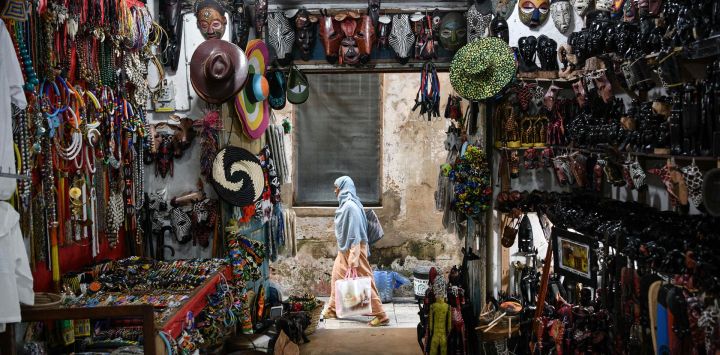 Imagen de una mujer caminando frente a una tienda de recuerdos, en el Stone Town de Zanzíbar, Tanzania. Reconocida por su impresionante belleza natural y su rica historia, Zanzíbar se ha convertido en un destino turístico popular en la región de Africa Oriental.