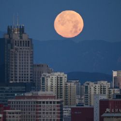 La luna se esconde tras los edificios de Pekín al amanecer. | Foto:Greg Baker / AFP