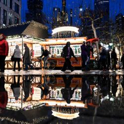 Las personas que visitan una feria navideña se reflejan en un estanque mientras se ve el horizonte con los edificios del distrito bancario en el centro de Frankfurt am Main, oeste de Alemania. | Foto:KIRILL KUDRYAVTSEV / AFP