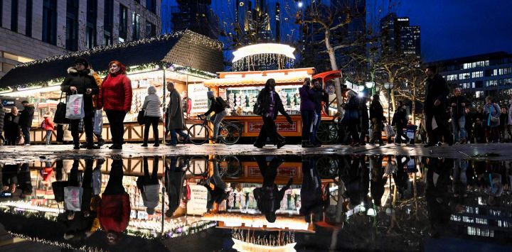 Las personas que visitan una feria navideña se reflejan en un estanque mientras se ve el horizonte con los edificios del distrito bancario en el centro de Frankfurt am Main, oeste de Alemania.