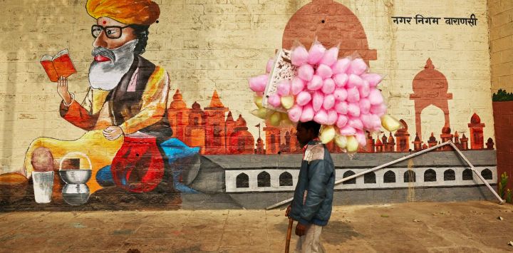 Un vendedor de algodón de azúcar pasa junto a un mural en las orillas del río Ganges en Bundiparkota Ghat en una fría mañana de invierno en Varanasi, India.