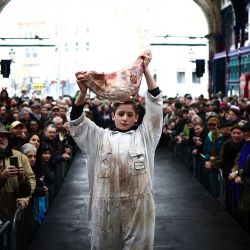 Un joven carnicero muestra un corte de carne a los clientes durante la tradicional subasta de carne de Nochebuena en el mercado de carne de Smithfield, en la ciudad de Londres. | Foto:HENRY NICHOLLS / AFP