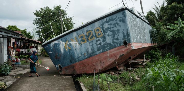 Syafriani, de 41 años, cuya madre sigue desaparecida tras el tsunami del océano Índico de 2004, limpia delante de su casa, donde dos patrulleras encallaron y permanecen preservadas por deseo de la comunidad, en Banda Aceh, en vísperas del aniversario del tsunami.