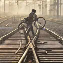 Un hombre lleva su bicicleta mientras cruza una vía férrea en una mañana invernal cerca de una estación de tren en Jalandhar, India. | Foto:Shammi Mehra / AFP